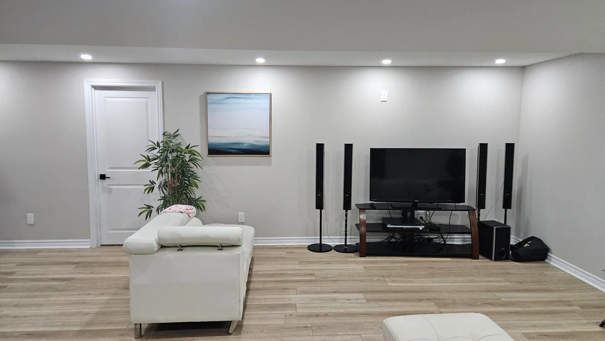 Wide finished basement lounge with television area and pale wood-look flooring