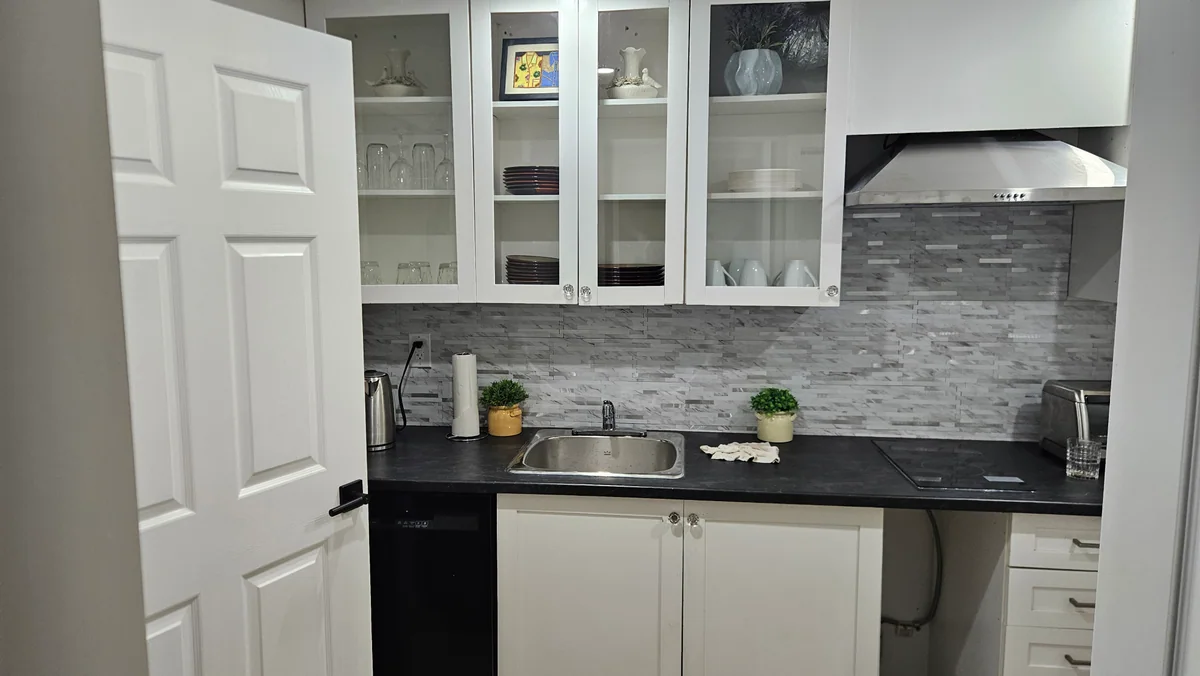 Finished basement wet bar with white cabinets and dark countertop
